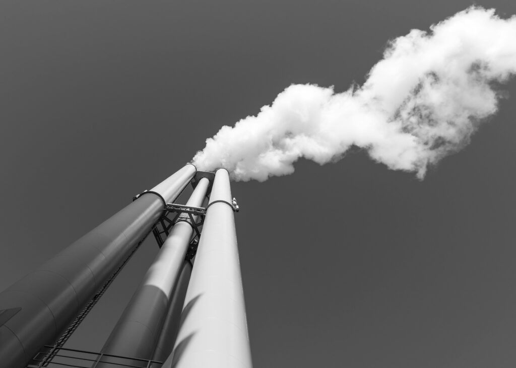 Black and white image of a smokestack with smoke against a clear sky in Hamburg.