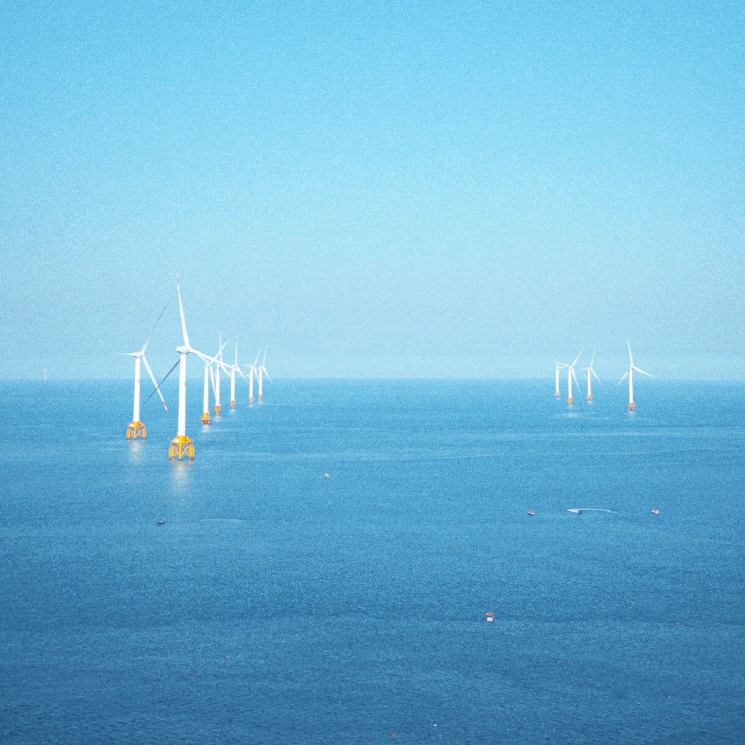 A serene view of wind turbines in the ocean under a clear blue sky, symbolizing renewable energy.